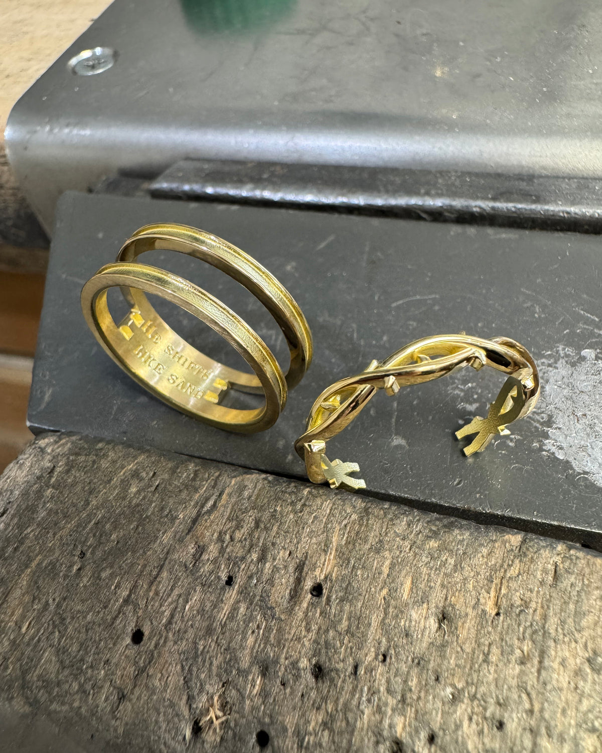 Gold ring components on a dark metal surface over a rustic wooden workbench.